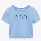 Drie maal de Geborduurde dolfijn strijkpatch met speels ontwerp op een lichtblauw t-shirtje