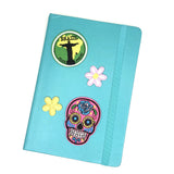 Neon Roze Sugar Skull Strijk Embleem Patch samen met een Brazil en twee bloem patches op de voorzijde van een blauwe agenda