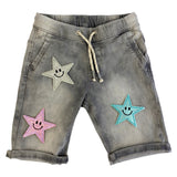 Zilverkleurige Smiley Glitter Ster Strijk Embleem Patch samen met twee andere glitters smiley sterren op een grijze kortebroek