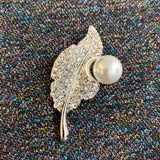 Zilverkleurig Blad Versierd Met Strass En Parel Broche Speld op een  stoffen achtergrond met glitter garen